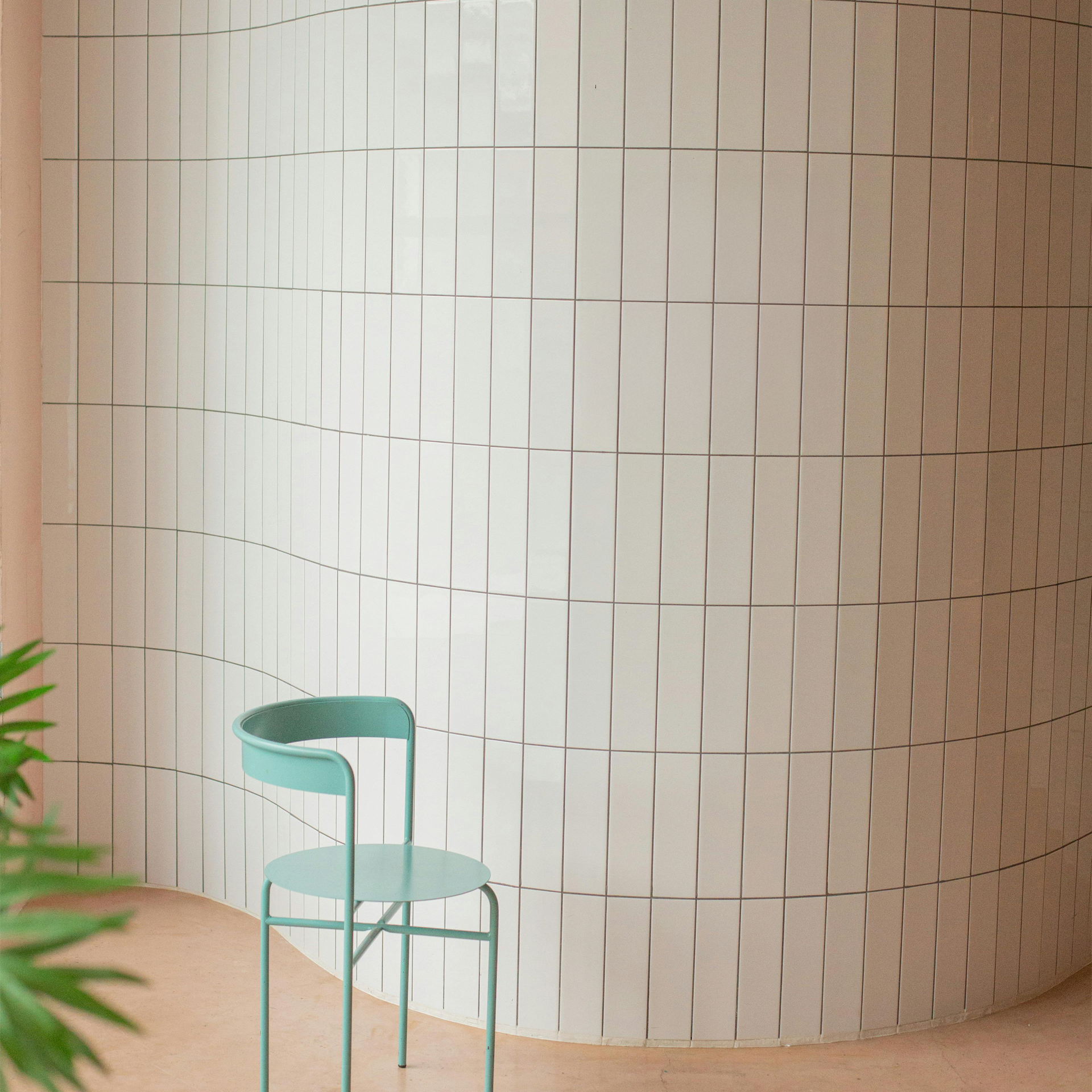 Green chair against a wall with vertical white tiles on a beige background